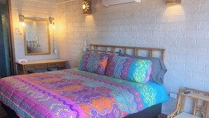 Een kamer met een bed, een bankje, een wandairconditioner en een bakstenen muur.