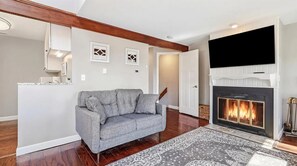 Ein Wohnzimmer mit Kamin, einem grauen Sofa und einem gemusterten Teppich.
