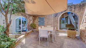 An outdoor patio with a table and chairs, a stone wall, and a view of a staircase. - Wonderful 4BR Farmhouse with Private Pool (Rabat)