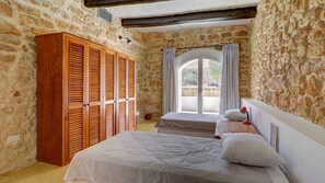 A bedroom with stone walls, a wooden wardrobe, a bed with a white duvet, and a window with curtains. - Wonderful 4BR Farmhouse with Private Pool (Rabat)