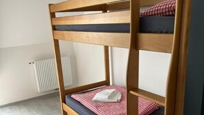 A bunk bed with a checkered bedspread and pillows, a radiator, and a light-colored wooden floor. - Auberge du Graber (Dolleren)