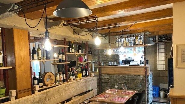 A restaurant with wooden tables, wine bottles, and a bar area. - Auberge du Graber (Dolleren)