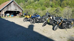 Motorcycles parked in front of a wooden building with a gravel driveway. - Auberge du Graber (Dolleren)