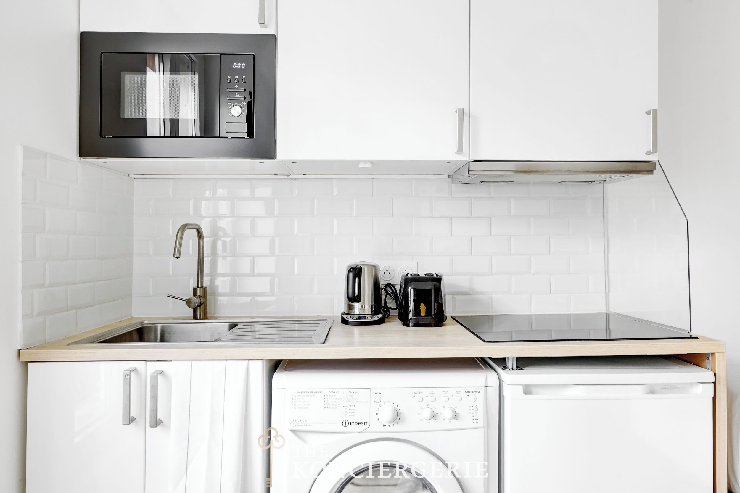 A compact kitchen with a microwave, coffee maker, toaster, sink, and a washing machine.