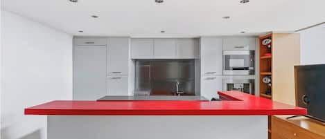 Uma cozinha moderna com bancada vermelha, eletrodomésticos de aço inoxidável e armários brancos.