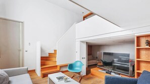 Ein modernes Wohnzimmer mit Treppe, Flachbildfernseher, blauem Sessel und Couchtisch.