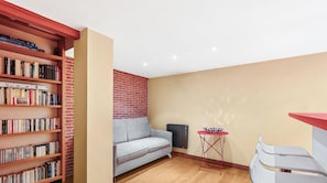 Ein gemütliches Zimmer mit Bücherregal, grauem Sofa, kleinem Tisch und Heizkörper.