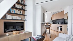 Ein zeitgemäßer Wohnraum mit integriertem Fernseher, Bücherregalen, Essbereich und Küche.