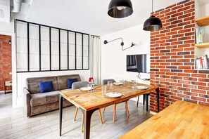Ein modernes Wohnzimmer mit einem Holzesstisch, gedeckt für sechs Personen, einer Couch, einer Ziegelwand und einem großen Fenster.