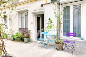Eine kleine Terrasse im Freien mit einem blauen Klapptisch und Stühlen, Blumentöpfen und einer Schmetterlingsdekoration an der Wand.