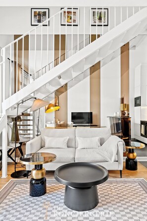 Ein modernes Wohnzimmer mit weißer Treppe, einem Sofa, einem Couchtisch und einem Fernseher.