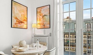 Ein Essbereich mit einem runden Tisch, Stühlen, einer Vase und einer Lampe. An der Wand hängen zwei abstrakte Gemälde.