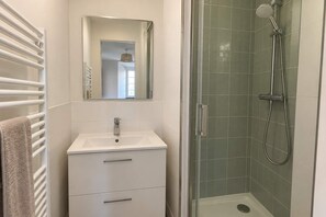 A bathroom with a white sink, a mirror, a towel rack, and a glass-enclosed shower area. - BM – Studio de charme près du Luxembourg (Paris)