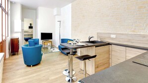 Een moderne keuken met een stenen muur, een bar met krukken, en een zithoek met een blauwe bank en een televisie.