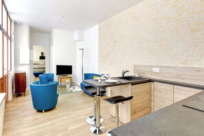 Une cuisine moderne avec un mur en pierre, un coin bar avec des tabourets, et un espace de vie avec un canapé bleu et un téléviseur.