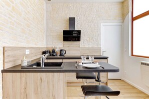 Une cuisine moderne avec un mur en pierre, une hotte noire et un coin repas comprenant une table et des chaises.