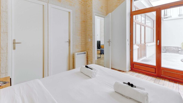 Een hotelkamer met een groot bed, witte lakens, een houten deur en uitzicht door een glazen deur op een buitenruimte.