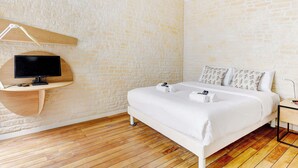 Een slaapkamer met een bed, een televisie op een houten standaard, een nachtkastje en een bakstenen muur.