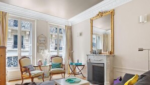 A living room with a fireplace, a large mirror, and a view of the street through large windows. - Elegance parisienne proche Opera et Montmartre (Paris)