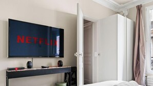 A room with a television displaying 'NETFLIX,' a bed, a door, and a window with curtains. - Elegance parisienne proche Opera et Montmartre (Paris)