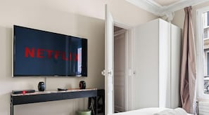 Ein Zimmer mit Fernseher, der 'NETFLIX' anzeigt, einem Bett, einer Tür und einem Vorhangfenster.