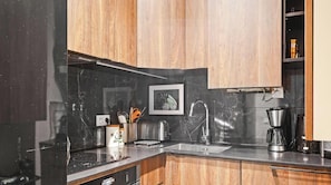Eine moderne Küche mit dunklen Arbeitsplatten, Holzschränken, einer Edelstahl-Spüle und einer Kaffeemaschine.
