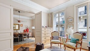 A room with a dining area, a large window with a view of buildings, and a door leading to another room. - Elegance parisienne proche Opera et Montmartre (Paris)