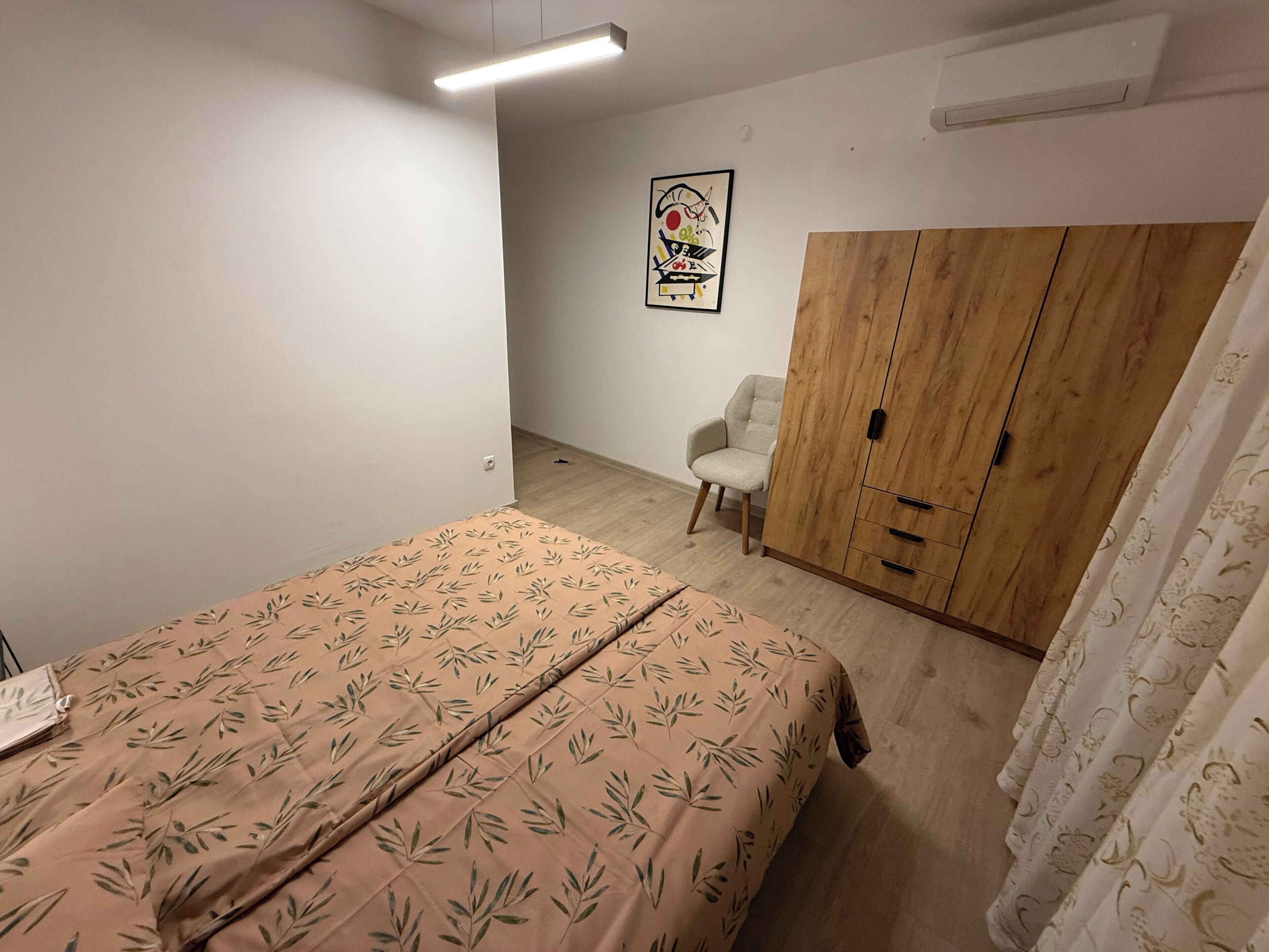 A bedroom with a bed, a wardrobe, a chair, and a wall-mounted artwork.