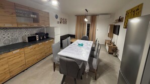 Eine moderne Küche mit Holzschränken, einem Esstisch mit Stühlen, einem Kühlschrank und einem an der Wand befestigten Fernseher.