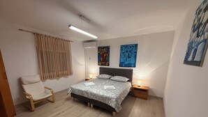 Ein Schlafzimmer mit einem Bett, einem Sessel, einem Nachttisch, einer Wand-Klimaanlage und Kunstwerken.
