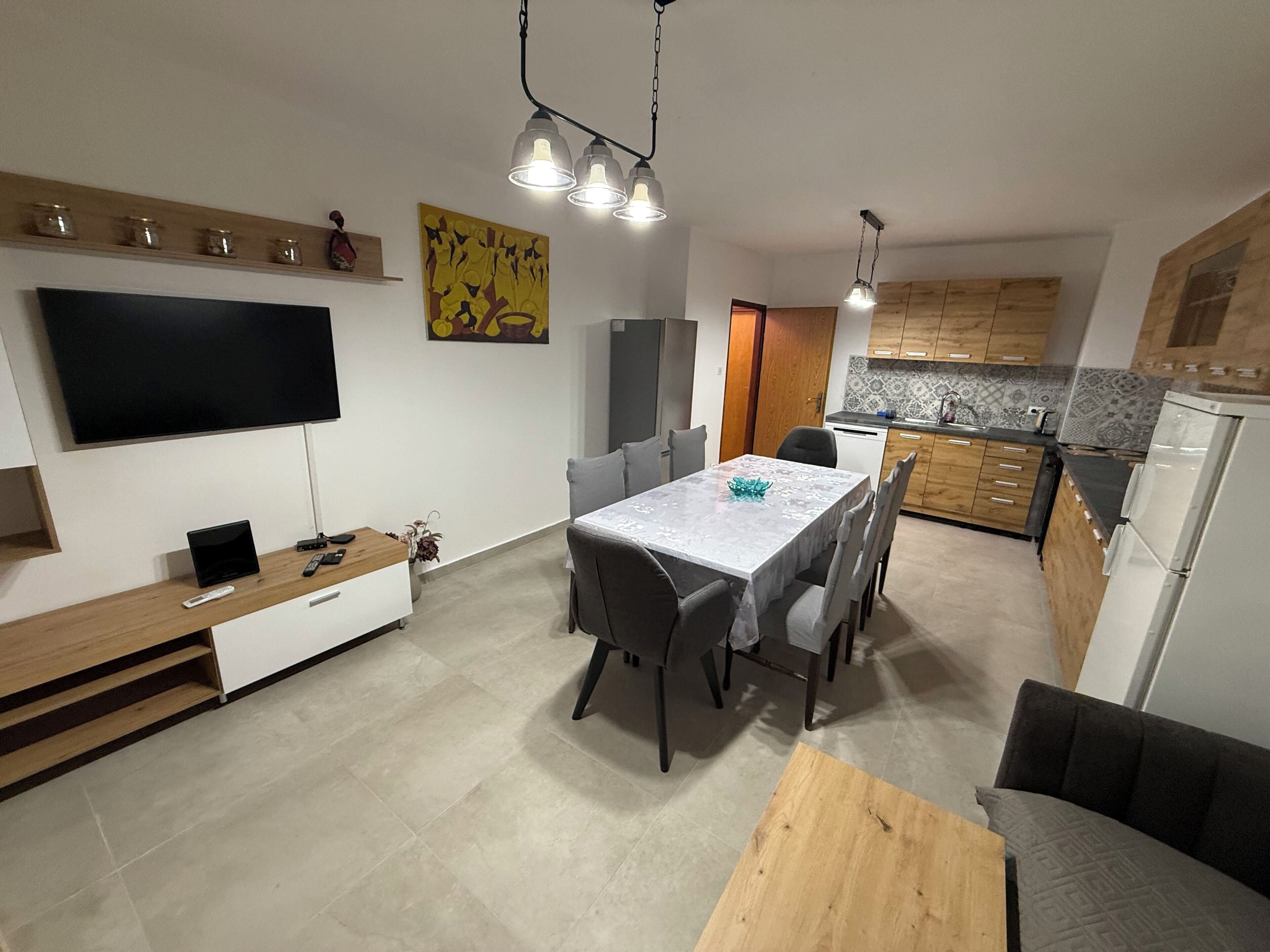 A modern kitchen with a dining area, a flat-screen TV, and a wooden dining table.