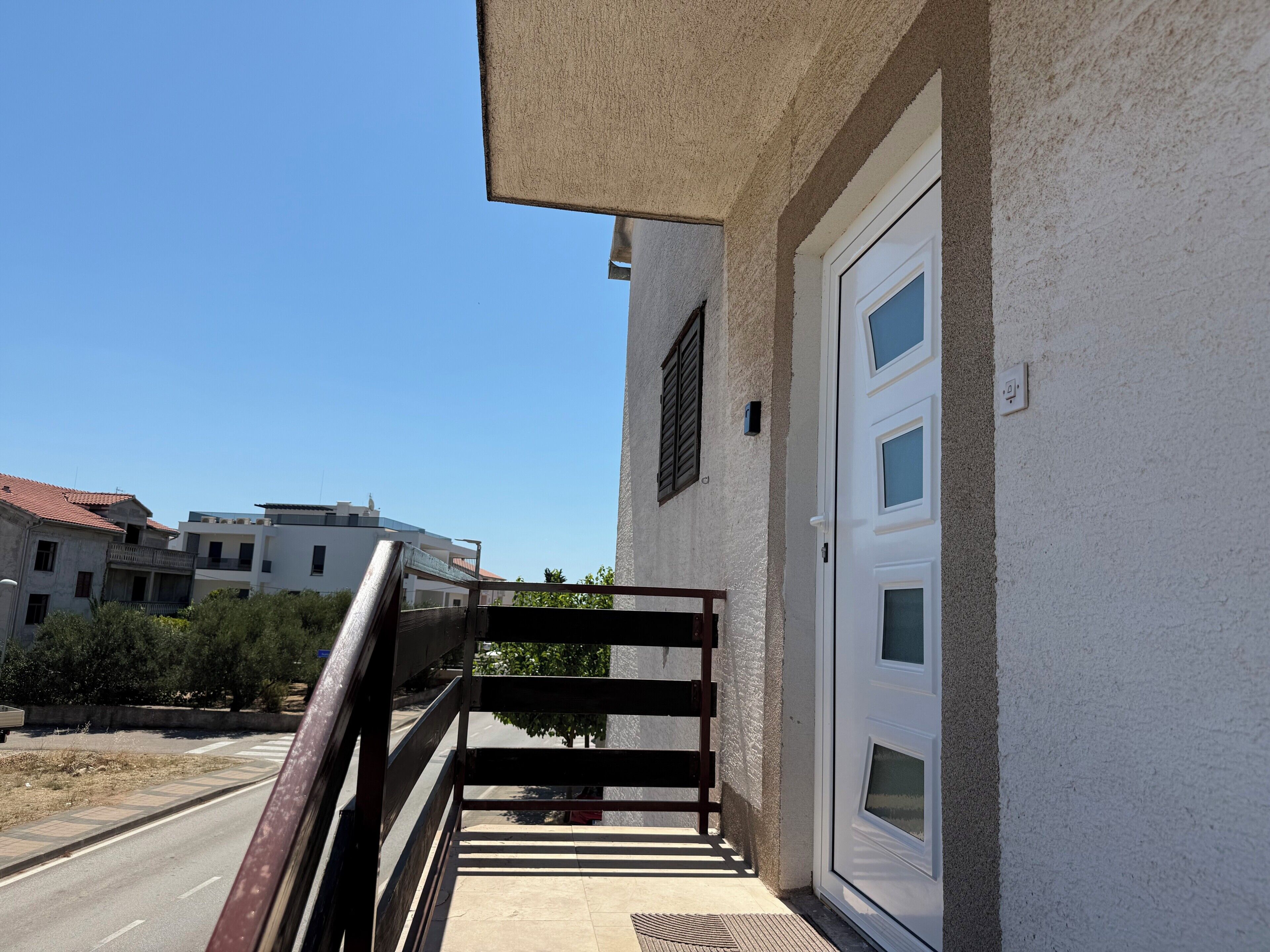 Ein Gebäude mit weißer Fassade, einer Glastür und einem Metallgeländer, das zu einem Balkon führt.