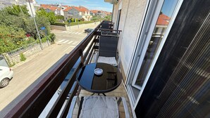 Ein Balkon mit Tisch und Stühlen, der auf eine Straße mit Häusern und einem parkenden Auto blickt.