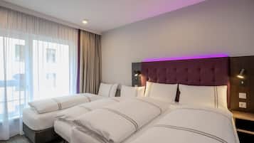 Habitación de hotel con dos camas, un ventanal con cortinas translúcidas, un cabecero moderno y una mesita de noche con lámpara.