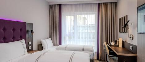 A hotel room with two beds, a desk, a TV, and a window with curtains.
