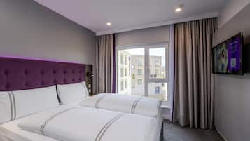 Una habitación de hotel con cama, cabecera, ventana con cortinas y un televisor instalado en la pared.
