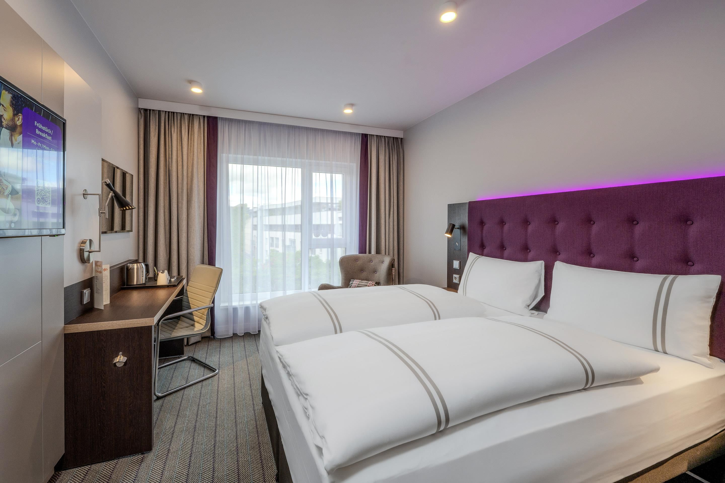 A hotel room with a bed, a desk, a chair, and a window with curtains.