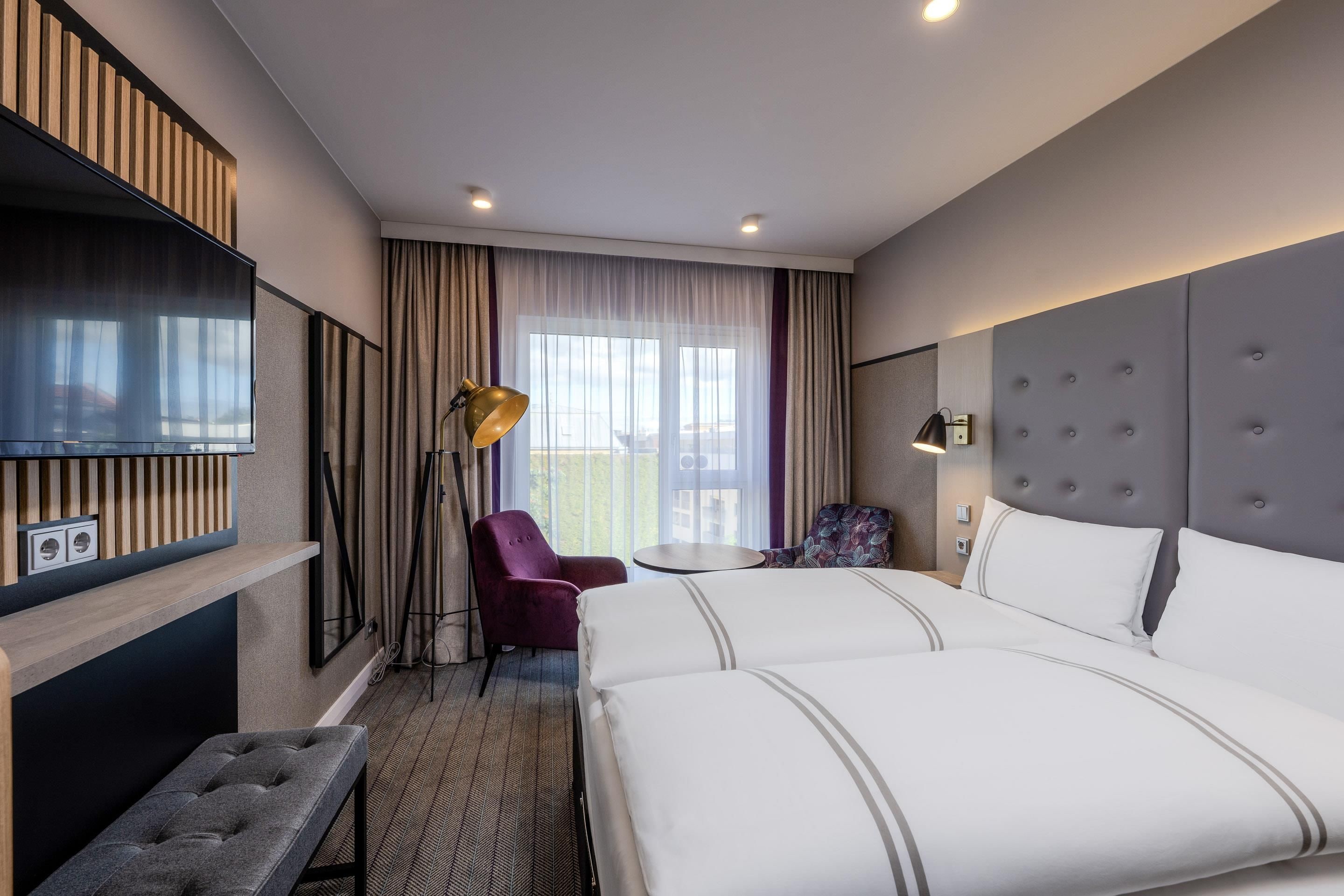 Een hotelkamer met een bed, een bureau, een stoel, een televisie en een raam met gordijnen.