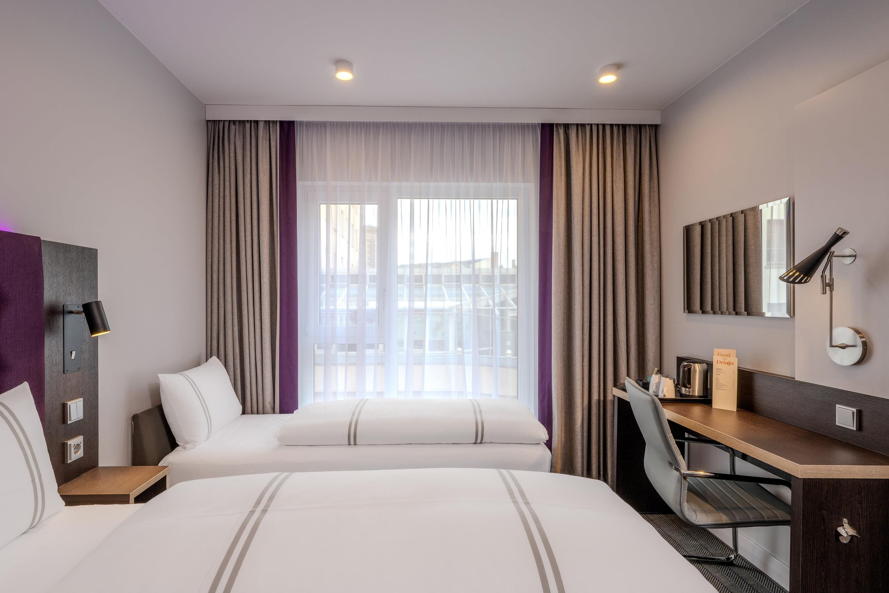 Habitación de hotel con dos camas, un escritorio, una silla, un espejo y una ventana con cortinas.