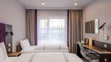 A hotel room with two beds, a desk, a chair, a mirror, and a window with curtains.