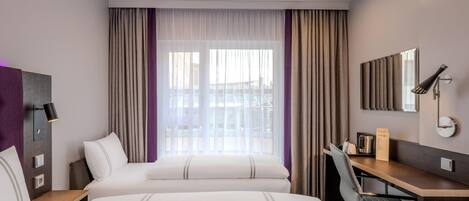 Habitación de hotel con dos camas, un escritorio, una silla, un espejo y una ventana con cortinas.