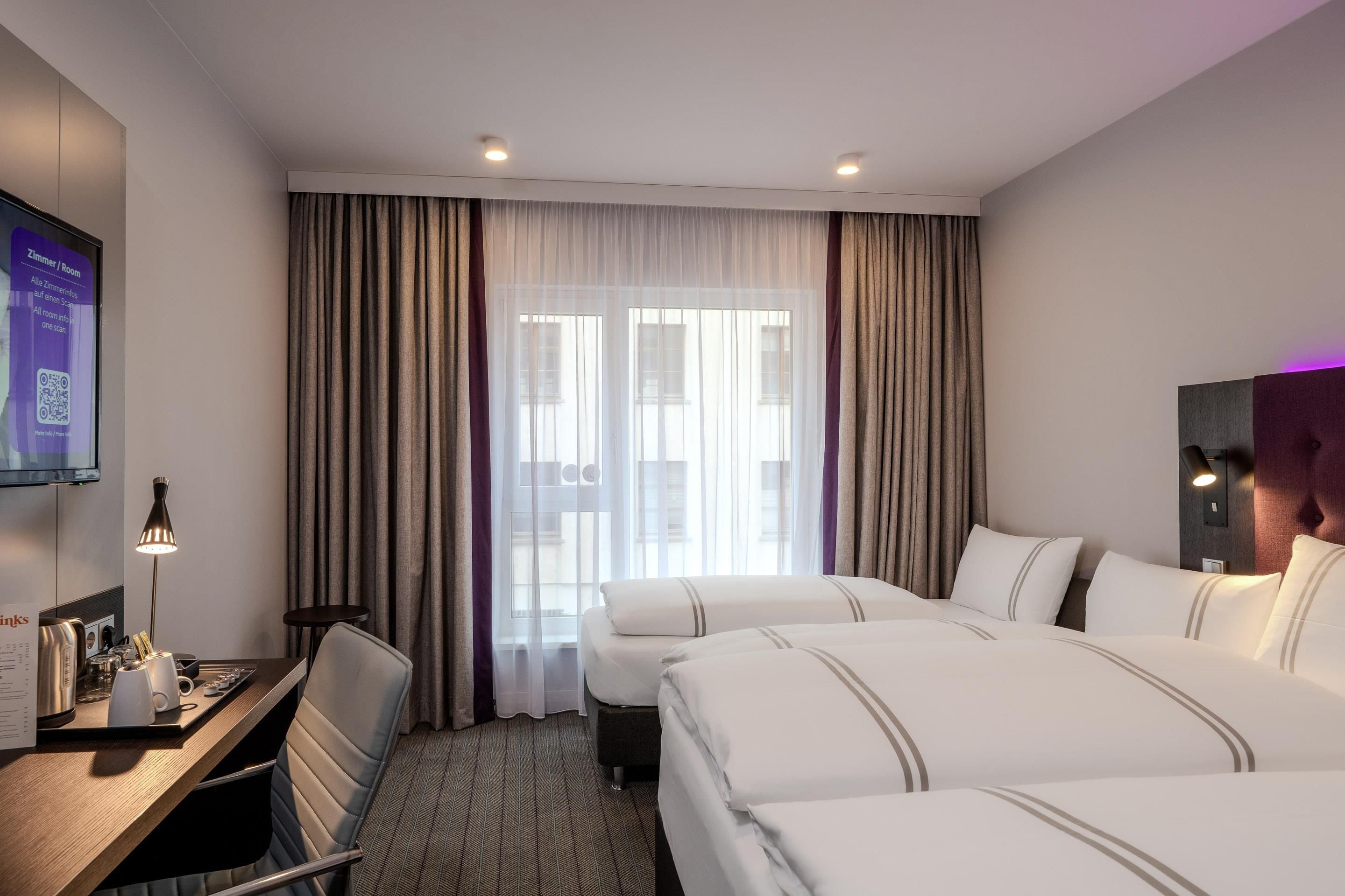 A hotel room with a desk, two beds, a TV, and a window with curtains.