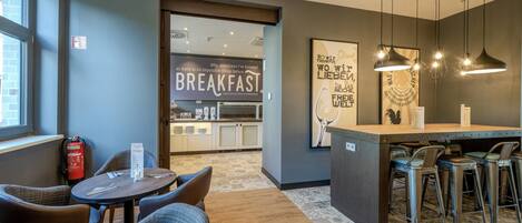 Espaço moderno para o café da manhã, com balcão, assentos e uma placa com a inscrição 'BREAKFAST'.