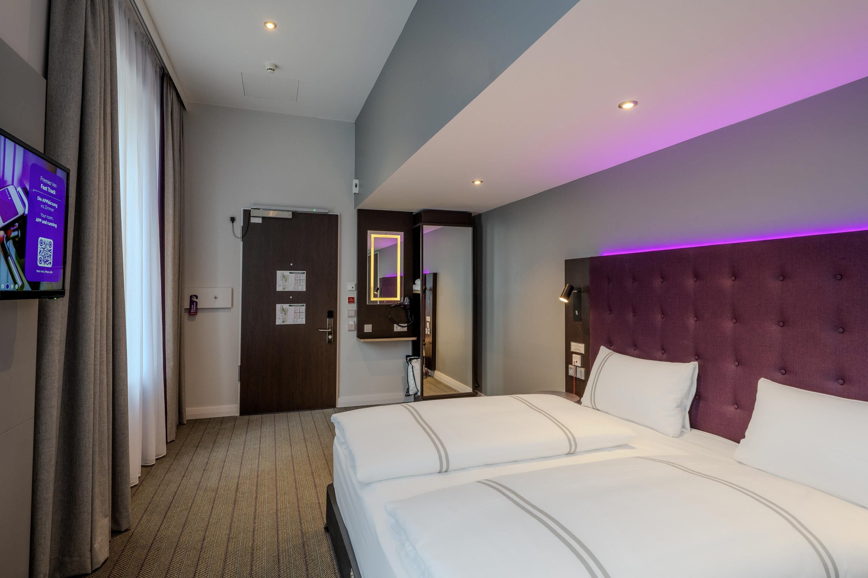 Habitación de hotel con una cama grande, un televisor de pantalla plana montado en la pared y una puerta que da a otra habitación.