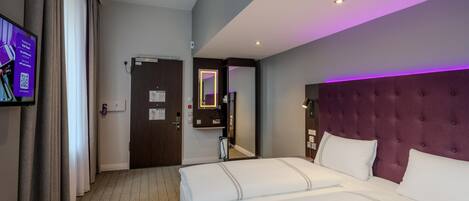 Habitación de hotel con una cama grande, un televisor de pantalla plana montado en la pared y una puerta que da a otra habitación.