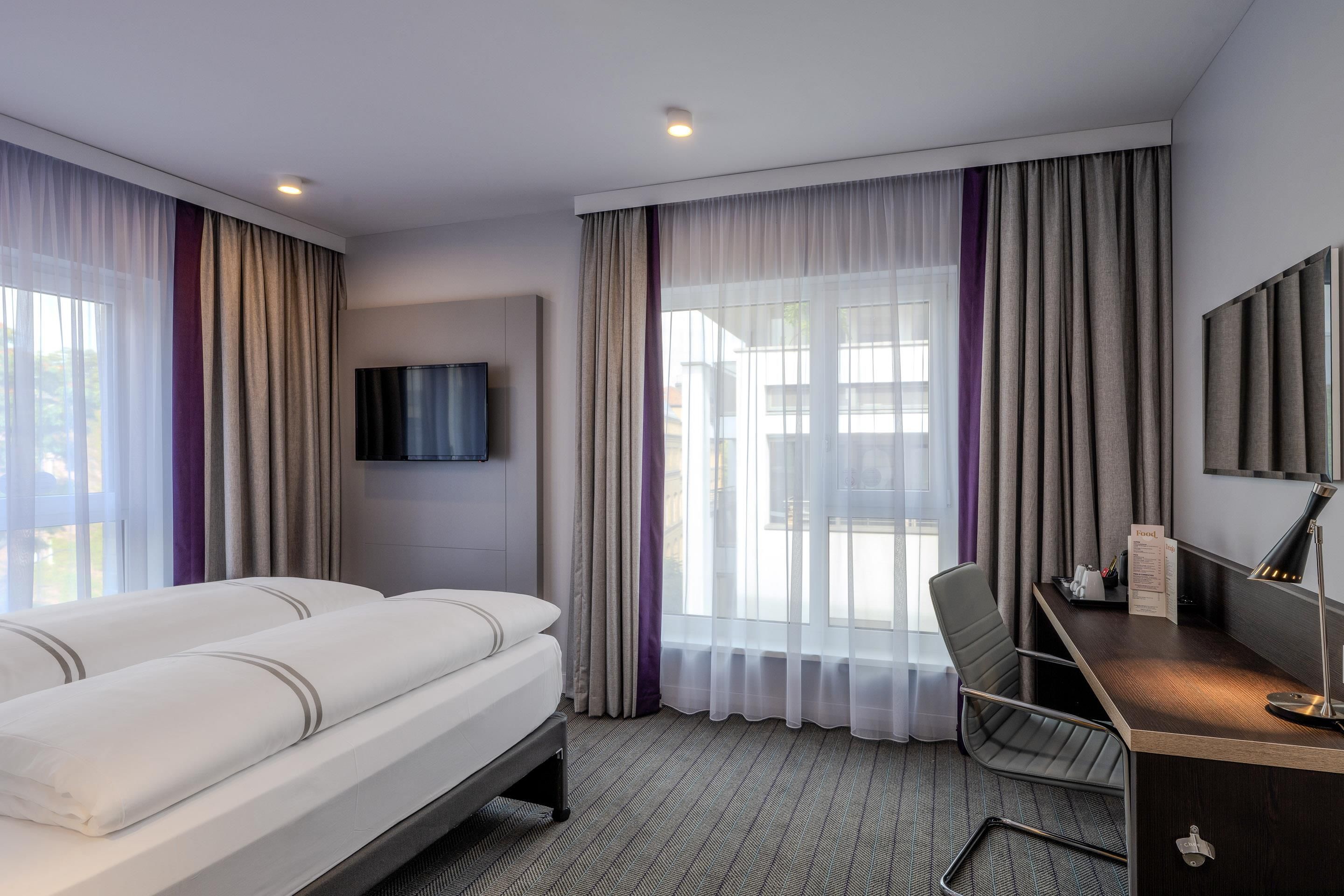 A hotel room with a bed, a desk, a chair, a television, and a window with curtains.