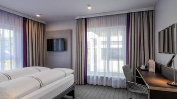 A hotel room with a bed, a desk, a chair, a television, and a window with curtains.