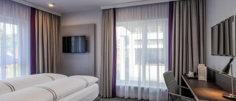 A hotel room with a bed, a desk, a chair, a television, and a window with curtains.