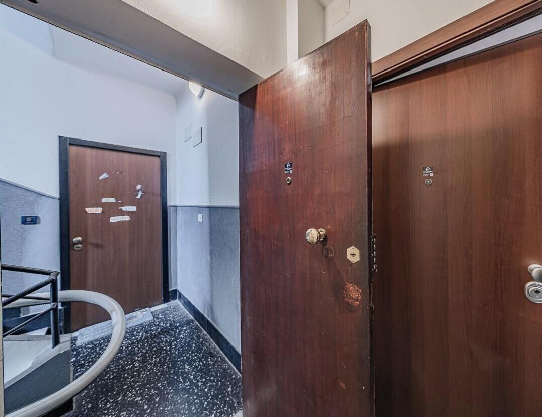 Un corridoio con una porta in legno, una ringhiera metallica e un pavimento piastrellato.