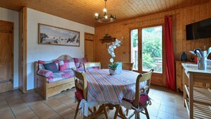 A wooden cabin interior with a dining table, chairs, a sofa, a chandelier, and a television. - Ground-Floor Apartment for 4, 50 m from the Slopes in La Clusaz (La Clusaz)